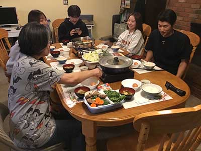 Japanese ESL students, with host mother, gather for skiyaki