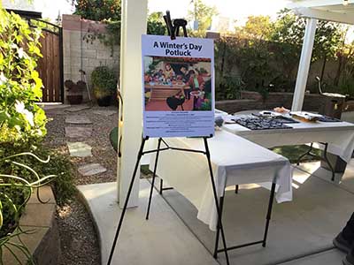 potluck dinner event poster on an easel in back yard