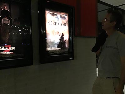 Lance looking at a backlit poster for the movie The Creator